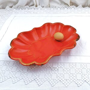May include: A bright orange, scalloped metal serving dish with a gold rim. An egg is sitting in the centre of the dish.