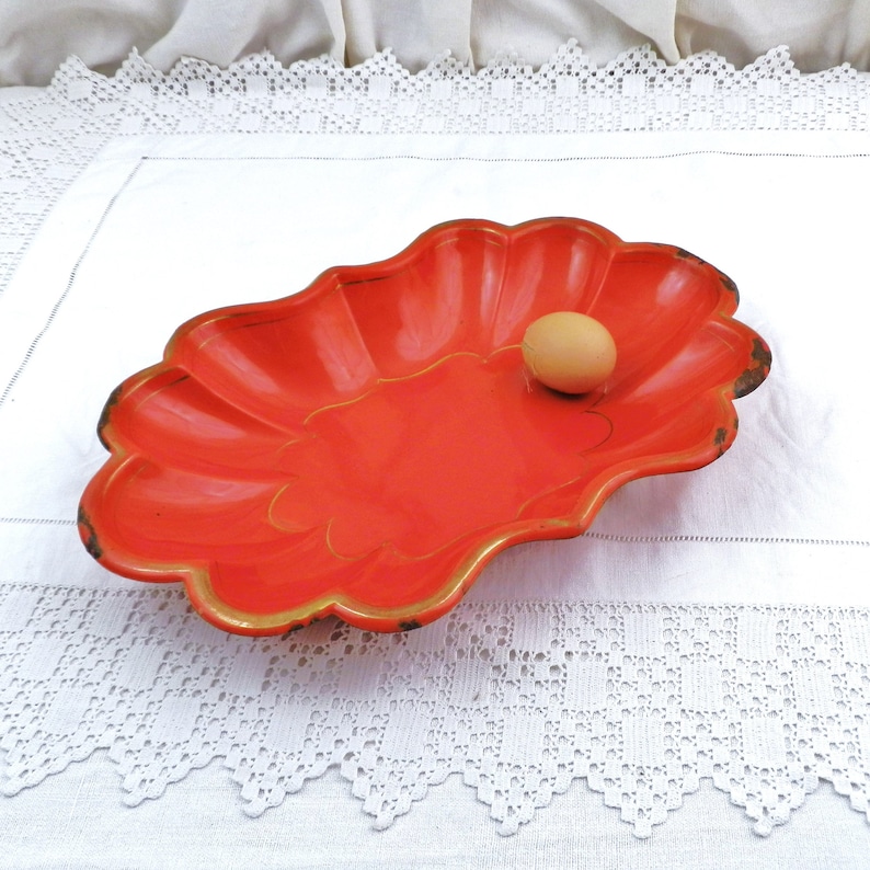 May include: A bright orange, scalloped metal serving dish with a gold rim. An egg is sitting in the centre of the dish.
