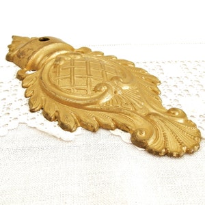May include: A gold-toned metal decorative accent with a detailed, ornate design. The accent features a central, raised, geometric pattern surrounded by intricate scrollwork and leaf motifs.