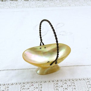 May include: A small, oval-shaped, iridescent mother-of-pearl bowl with a twisted wire handle. The bowl is on a white surface.