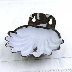 Può includere: Un portasapone da parete vintage bianco con bordo smerlato e finiture marrone ruggine. Il piatto ha un design a forma di conchiglia e una staffa con due fori per appenderlo.