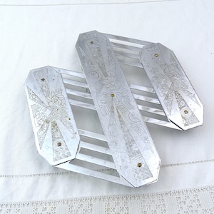 May include: Silver-toned metal hot pad with an intricate geometric design. The pad is made of interwoven metal strips and has a decorative pattern on each of the three sections.