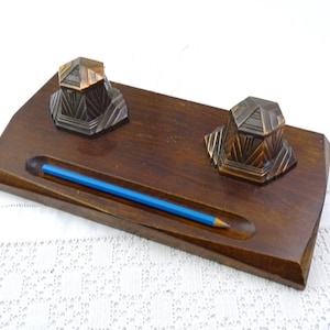 Puede incluir: Un organizador de escritorio de madera con dos tinteros y un porta lápices. Los tinteros son de metal y tienen un diseño geométrico. El porta lápices es de madera y tiene una ranura para el lápiz.