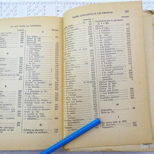 Pode incluir: Um livro de cozinha vintage aberto com um l&aacute;pis azul na p&aacute;gina. O livro &eacute; intitulado "Table Alphabetique des Recettes" e lista v&aacute;rias receitas em franc&ecirc;s.