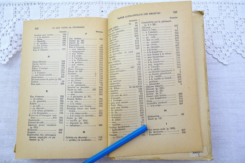 Pode incluir: Um livro de cozinha vintage aberto com um l&aacute;pis azul na p&aacute;gina. O livro &eacute; intitulado "Table Alphabetique des Recettes" e lista v&aacute;rias receitas em franc&ecirc;s.