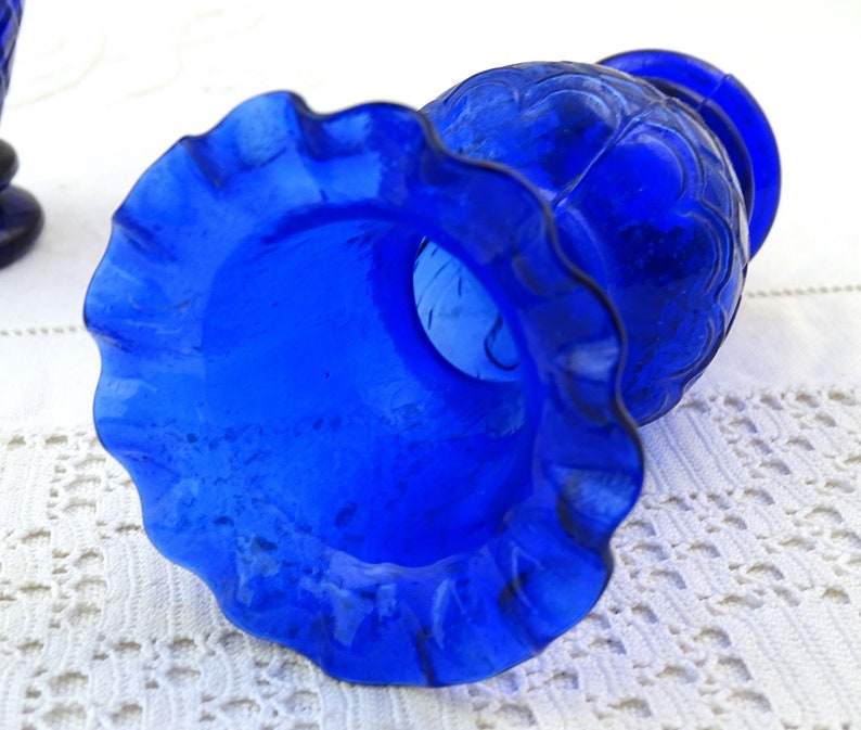 May include: A cobalt blue glass vase with a ruffled rim and a textured design. The vase is empty and appears to be vintage.