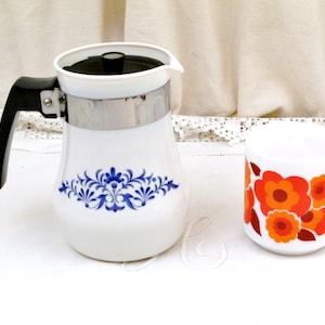 Peut inclure: Une cafetière blanche avec un motif floral bleu et une poignée noire. À côté se trouve une tasse blanche avec un motif floral rouge et orange.