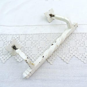 Puede incluir: Manija de puerta blanca, desgastada, de estilo vintage, con un centro retorcido y placas de montaje en forma de estrella. El tirador es de madera y metal, con desgaste visible, lo que sugiere un aspecto antiguo o rústico.