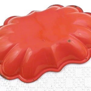 May include: Orange metal mould with a scalloped edge. The mould is shaped like a flower with five petals.