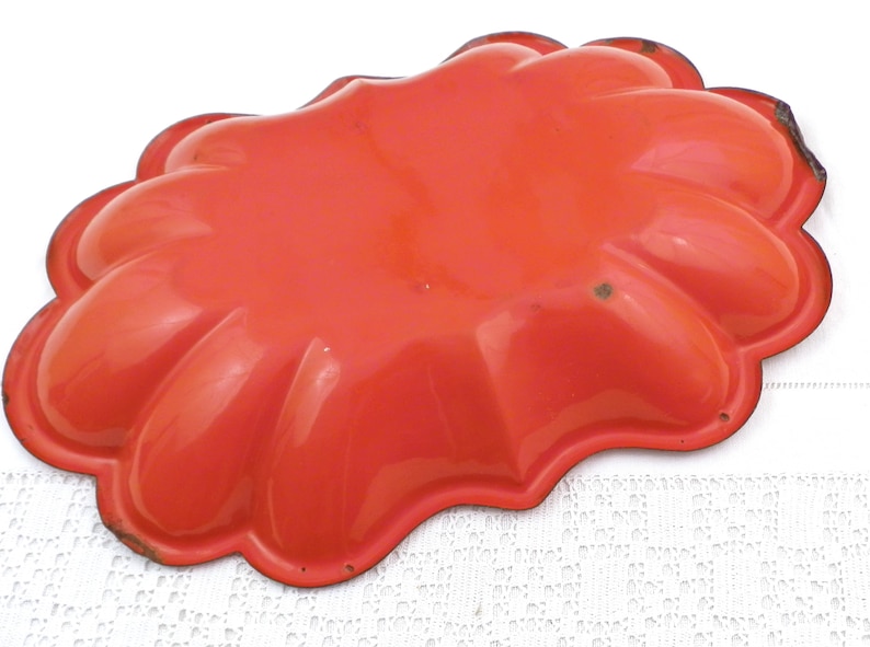 May include: Orange metal mould with a scalloped edge. The mould is shaped like a flower with five petals.