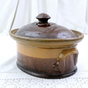 Può includere: Una pirofila in ceramica ovale con coperchio. Il piatto presenta un design bicolore marrone e beige. Ha manici laterali e un piccolo pomello sul coperchio. Adatto per cuocere al forno e servire, è un elemento essenziale in cucina.