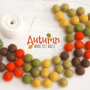 Peut inclure: Une collection de boules de feutre de laine colorées dans des tons de brun, orange, jaune et vert. Les boules de feutre sont disposées en cercle autour d'une pelote de fil blanc et d'une pièce de feutre en forme de cœur. Le texte "Autumn Wool Felt Balls" est écrit au centre de l'image.