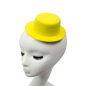 May include: A white mannequin head with closed eyes wearing a small, bright yellow hat.