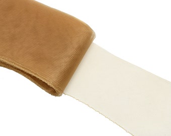 Può includere: Un rotolo di tessuto tulle color oro. Il tessuto è trasparente e ha una texture delicata.