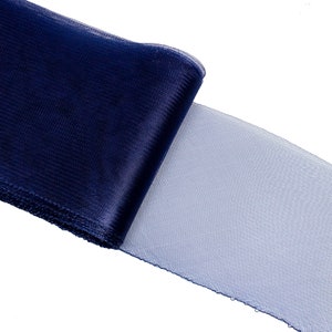 May include: A roll of navy blue tulle fabric. The fabric is partially unrolled, revealing a lighter blue, sheer material. The tulle has a fine, open weave, and the edges are cleanly cut. The fabric is likely used for crafting or decorative purposes.