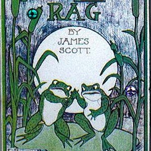 May include: A vintage sheet music page with the title "Frog Legs Rag" by James Scott. The page features two frogs sitting on lily pads in a pond. A gold frog pin is shown below the sheet music.