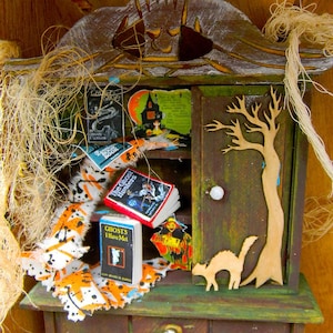 May include: A miniature wooden dollhouse hutch with a green and brown paint finish. The hutch has a shelf with several miniature books with Halloween themes, including "The Ghost Hunters" and "Ghosts I Have Met". There is a small black cat figurine and a wooden tree cutout on the hutch.