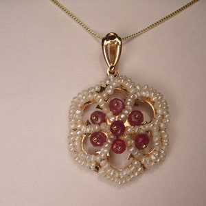 May include: A gold pendant necklace with a flower-shaped design. The pendant is made of small white pearls and features red gemstones in the centre of each flower petal.
