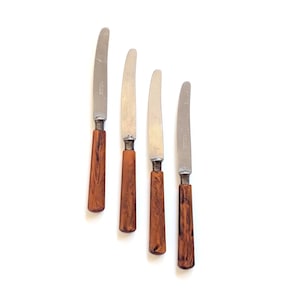 May include: Four vintage butter knives with stainless steel blades and brown, marbled handles. The knives are arranged diagonally against a white background, showcasing their classic design and potential for elegant table settings.