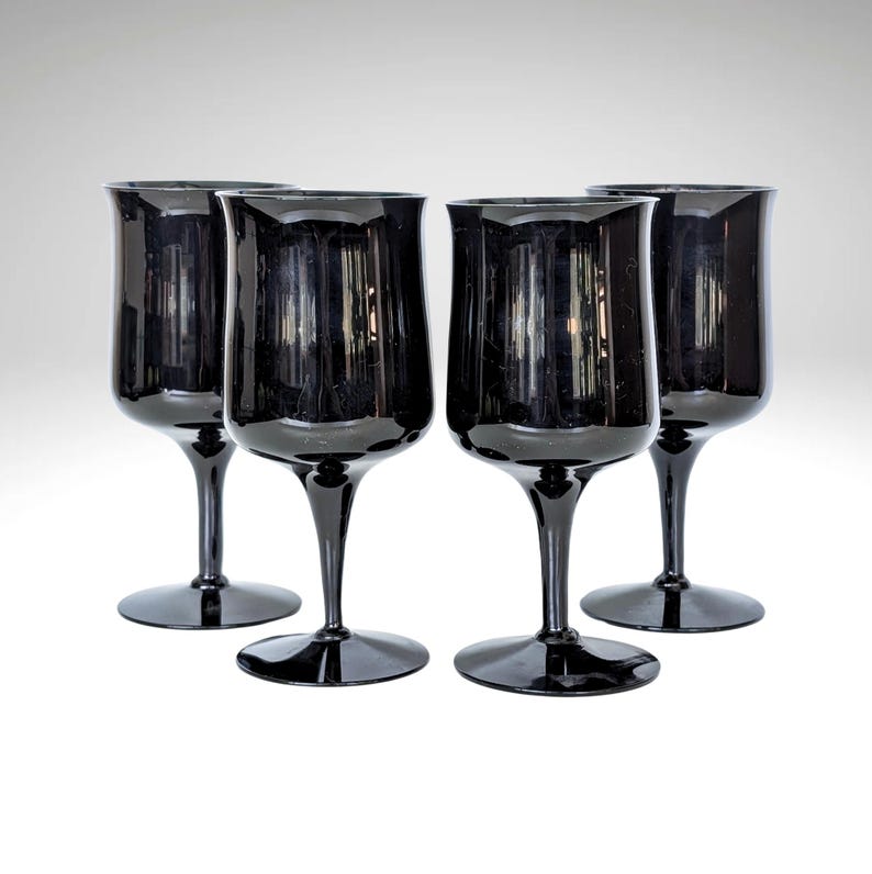 May include: Set of four black wine glasses with a wide bowl and a long stem. The glasses are made of clear glass and have a dark, almost black, tint.