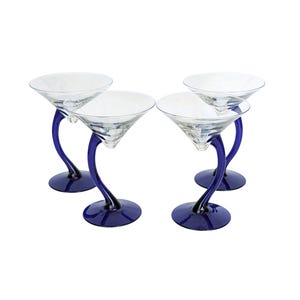 May include: A set of four clear glass martini glasses, each featuring a distinctive curved, cobalt blue stem and a matching circular blue base. The glasses have a wide, conical bowl shape designed for cocktails, with a smooth, transparent finish.