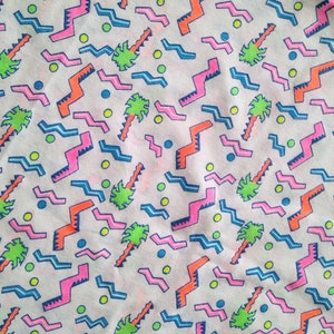 May include: A white fabric with a repeating pattern of pink, blue, and orange geometric shapes and green palm trees. The background is white with small yellow and blue dots.