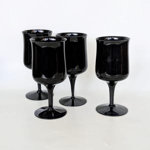 May include: Set of four black glass wine glasses. The glasses have a classic shape with a wide bowl and a long stem.