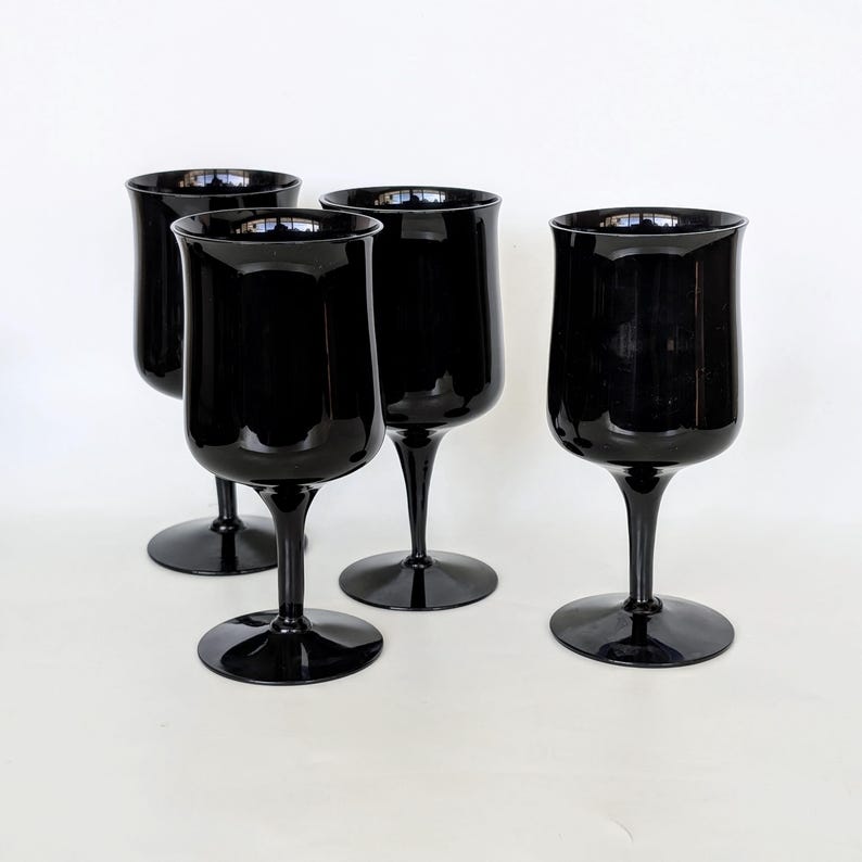 May include: Set of four black glass wine glasses. The glasses have a classic shape with a wide bowl and a long stem.