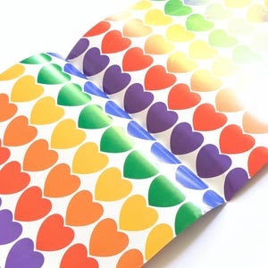 Pu&ograve; includere: Fogli di adesivi a forma di cuore arcobaleno. I cuori passano attraverso i colori dell'arcobaleno, dal rosso all'arancione, giallo, verde, blu e viola. Gli adesivi sono disposti in file e colonne su sfondo bianco.