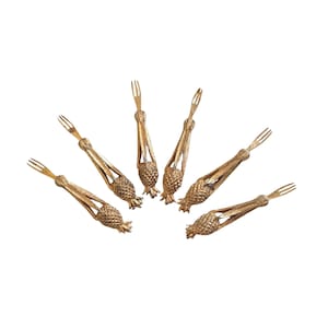 May include: Six gold-colored serving forks arranged in a semi-circle. Each fork has a pineapple-shaped handle and a three-pronged fork head. The forks are made of a metallic material and are set against a white background.