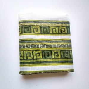 May include: White fabric with green and yellow geometric patterns. The fabric has a repeating pattern of a Greek key design.