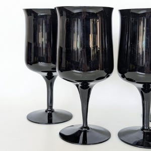 May include: Four black glass wine glasses with a wide bowl and a long, thin stem. The glasses are arranged in a row, with the front glass in focus.