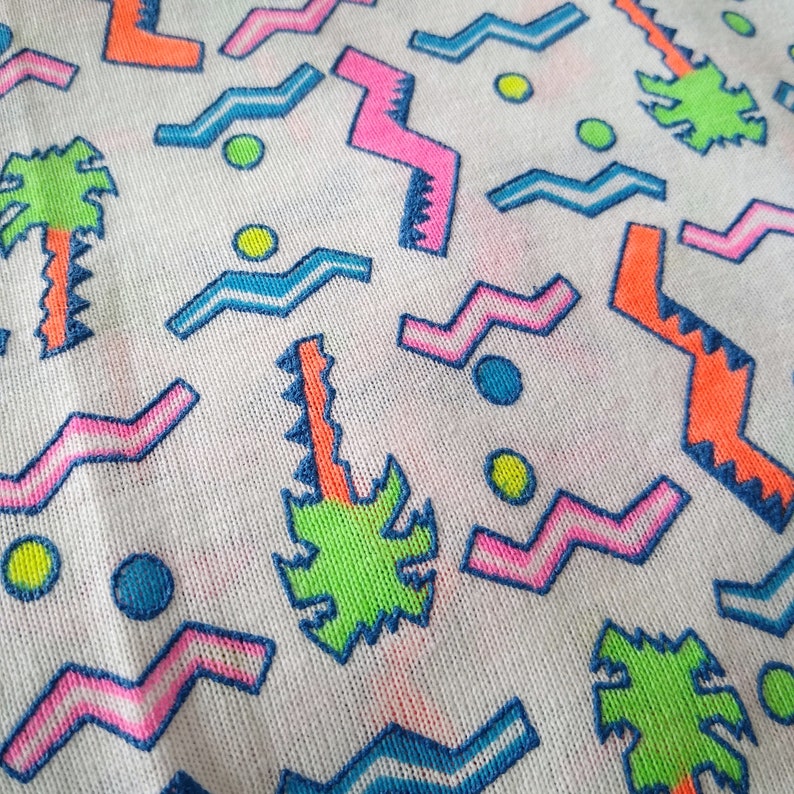 May include: White fabric with a colorful geometric pattern. The pattern includes zigzags, waves, and circles in pink, blue, green, and orange.