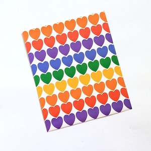 Pu&ograve; includere: Un taccuino rettangolare con un motivo ripetuto di cuori colorati in uno spettro arcobaleno. I cuori sono disposti in file e colonne su sfondo bianco. I colori includono arancione, rosso, viola, blu, verde e giallo.