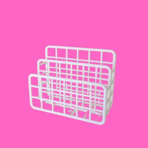 May include: A white plastic desk organizer with a grid-like design. The organizer has three sections for storing items. The background is a solid bright pink.