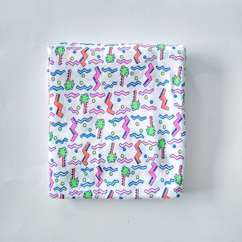 May include: White fabric with a repeating pattern of pink, blue, green, and orange palm trees, zigzags, and wavy lines.