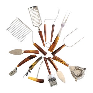 May include: A collection of vintage kitchen utensils with brown and amber-colored handles. The set includes a cheese grater, cake slicer, cheese knife, corkscrew, and a cocktail strainer. The metal components are silver-toned, and the arrangement is on a white background.