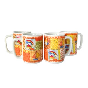 May include: Set of four white ceramic mugs with a patchwork design featuring a rainbow, houses, and sailboats. The mugs have orange, yellow, green, blue, and red accents.