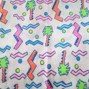 May include: A white fabric with a repeating pattern of pink, blue, green, and orange geometric shapes. The pattern includes zigzags, waves, and palm trees.