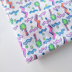 May include: White fabric with a repeating pattern of pink, blue, and orange zigzags, green palm trees, and yellow dots.