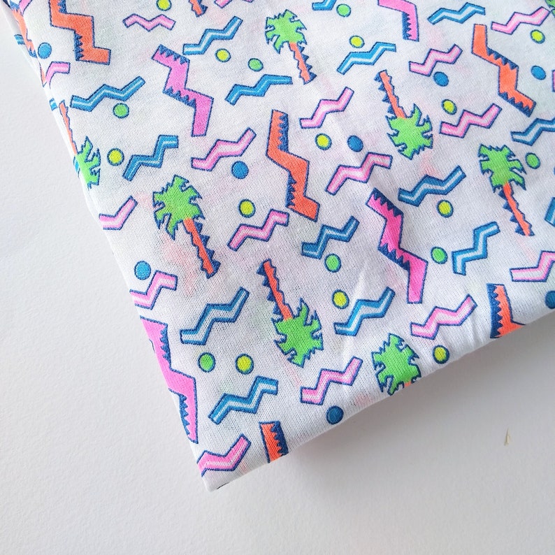 May include: White fabric with a repeating pattern of pink, blue, and orange zigzags, green palm trees, and yellow dots.
