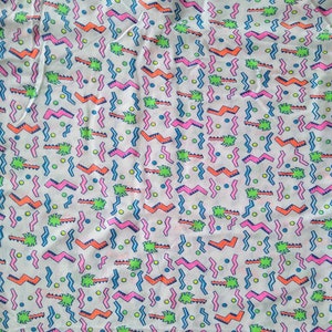 May include: A white fabric with a repeating pattern of pink, blue, green, and orange geometric shapes. The pattern includes zigzags, wavy lines, and small circles.