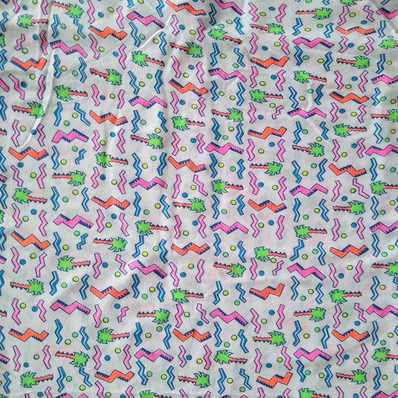 May include: A white fabric with a repeating pattern of pink, blue, green, and orange geometric shapes. The pattern includes zigzags, wavy lines, and small circles.