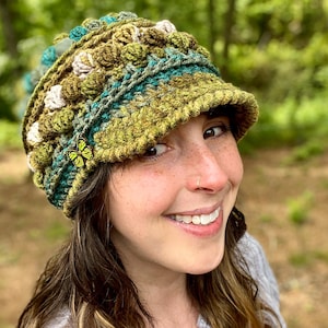 May include: A green, brown and blue crocheted hat with a wide brim and a butterfly pin. The hat has a textured, bumpy design.