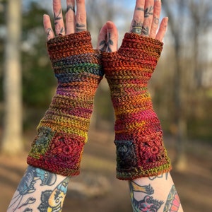 Pode incluir: Um par de luvas sem dedos de crochê coloridas com um design texturizado. As luvas são feitas com uma variedade de tons de vermelho, laranja, amarelo, verde e marrom.