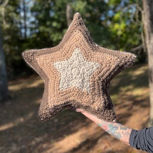May include: A brown and white star-shaped cushion with a textured surface. The cushion is made of yarn and has a fluffy appearance.