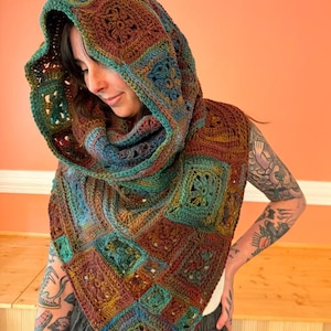 May include: A hooded cowl scarf constructed from multiple crocheted granny squares in a variegated color palette of deep brown, forest green, teal, and rust orange. The garment features a pointed front drape and a large, loose-fitting hood.