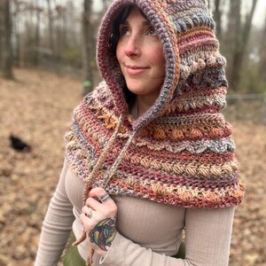 May include: A handmade crochet hood in shades of red, orange, brown, and gray. The hood features a textured pattern and a drawstring closure. The hood is designed to be worn around the neck and head, providing warmth and style.