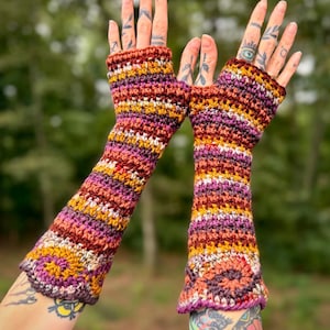 May include: A pair of fingerless gloves featuring a multi-colored crochet pattern with horizontal stripes in shades of deep purple, burnt orange, mustard yellow, and cream. The gloves extend from the knuckles to the mid-forearm with a textured stitch.
