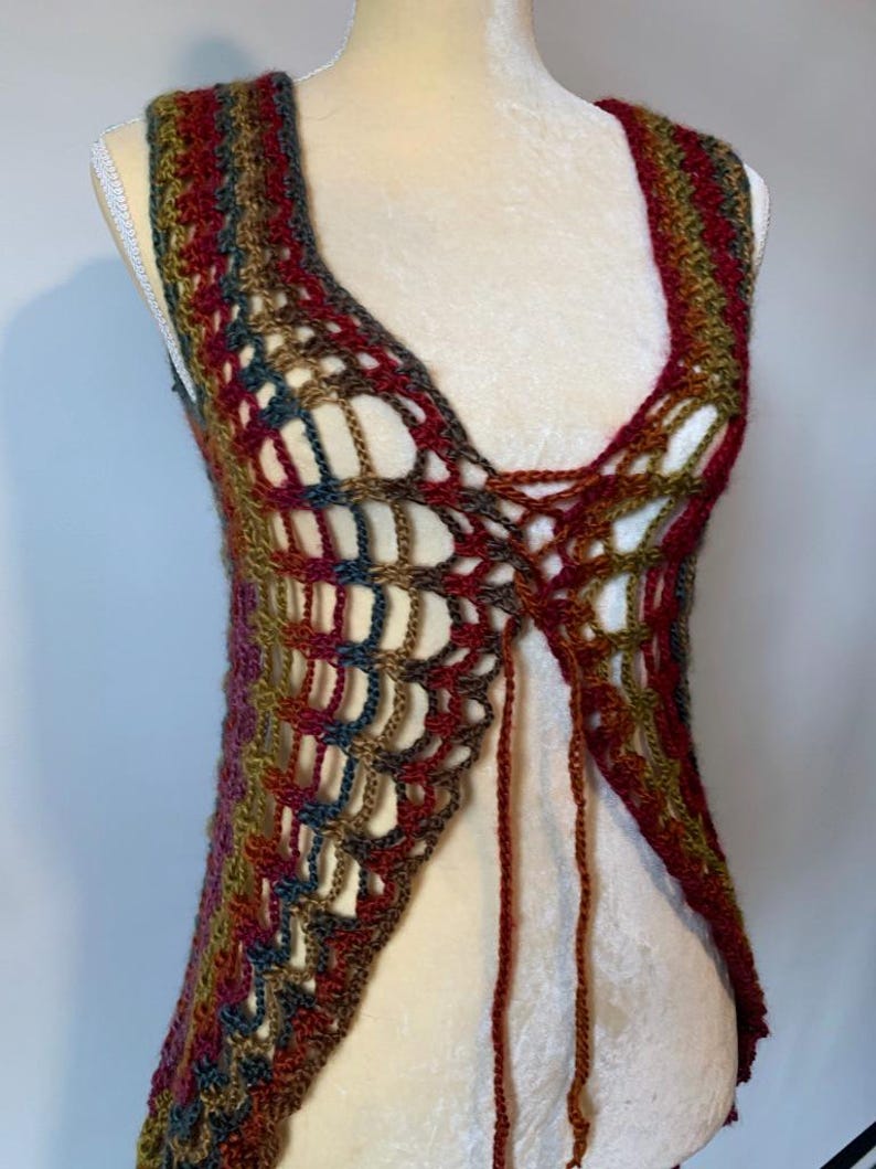 May include: A sleeveless crochet vest featuring an open, airy stitch pattern in a variegated color palette of deep red, olive green, dark blue, and brown. The garment has a V-neckline and includes long, thin yarn ties at the center front for closure.